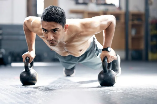 Fitness, push up or man with kettlebell for training, body workout or exercise at health club studio. Motivation, mindset or healthy Indian sports athlete exercising with focus or resilience at gym.
