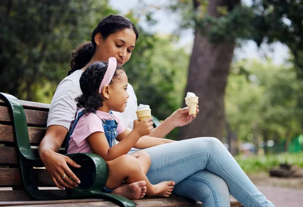 Summer, garden and ice cream with a mother and daughter bonding together while sitting on a bench outdoor in nature. Black family, children and park with a woman and girl enjoying a sweet snack.