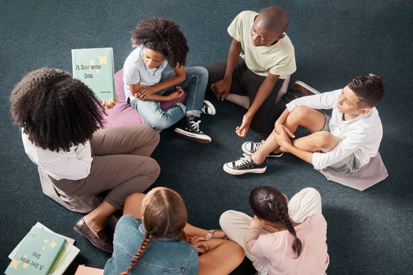 Teacher, storytelling or kids on classroom floor or library for learning development growth, listening skills. Top view, group or students with a black woman reading fun fantasy books st school.