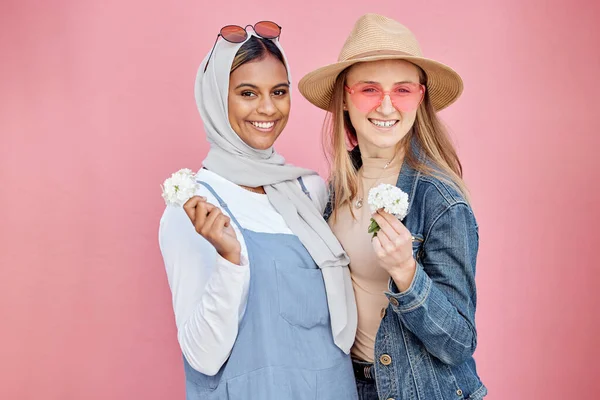 Friends, diversity and fashion women portrait with spring flowers on a pink background with a happy smile. Muslim woman and girl together for hug, love and support for lgbt freedom, respect and pride.