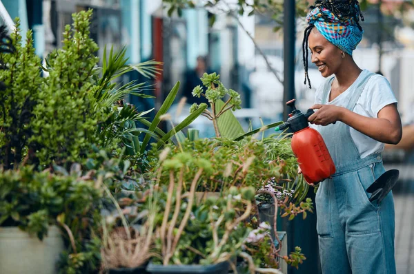 Water, flowers or black woman gardening in small business shop for healthy leaf or organic plants growth. Irrigation, store manager or girl entrepreneur watering floral agriculture with a happy smile.