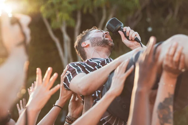 Crowd, surfing and man singing at party, outdoor music festival or social gathering. Microphone, energy and male singer diving in audience group at performance event, celebration or crazy fun weekend.
