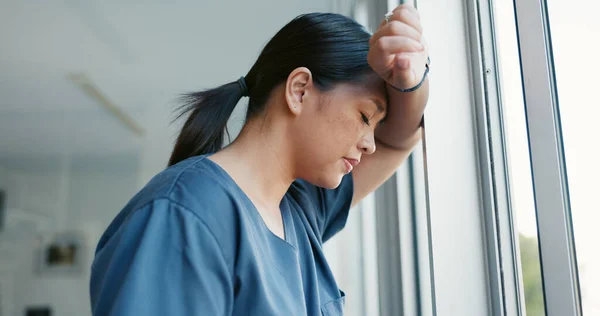 Healthcare nurse, stress and headache by window for working burnout, frustrated employee and tired asian woman in hospital. Doctor, pain and sad medical worker, anxiety or mental health depression.