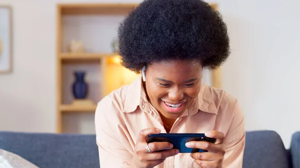 Excited online gamer excited about winning successful mobile game while relaxing at home. Young stylish female enjoying some online entertainment using a mobile device on a sofa in her house.