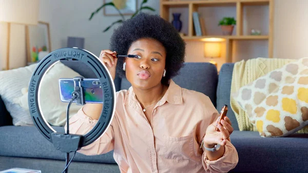 Afro beauty influencer, vlogger or podcast host talking, using phone to film live stream makeup tutorial with new mascara makeup. Excited woman using technology to promote cosmetic product from home.