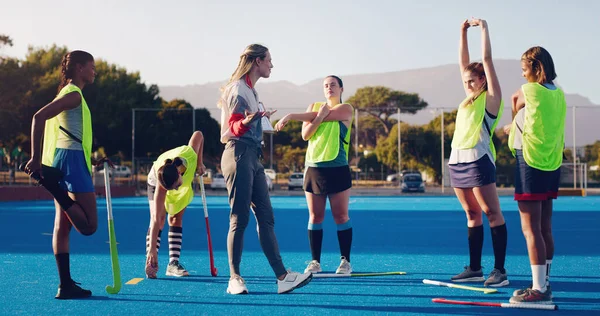 Hockey, women team with coach and sport outdoor, coaching and game strategy, training and fitness on turf. Athlete stretching, start practice and wellness with match plan, motivation and support.