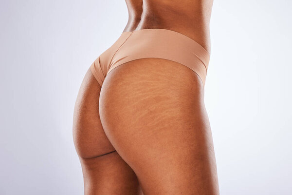 Cellulite, buttocks and underwear with a model black woman in studio on a gray background for body positivity. Stretch marks, real and natural with a female posing in lingerie from the back.