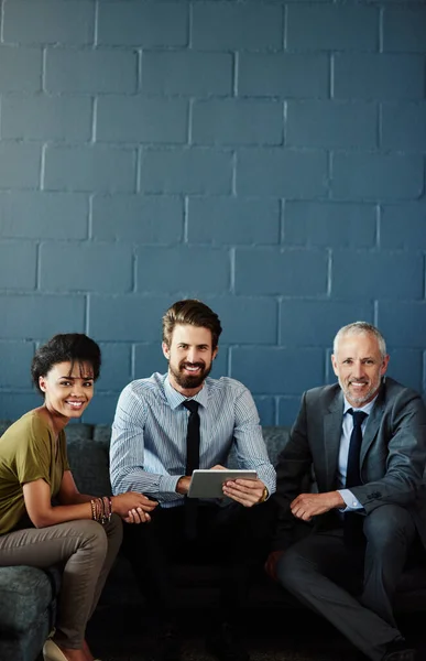 Let us help you achieve success. Cropped portrait of three businesspeople working together on a digital tablet in their office