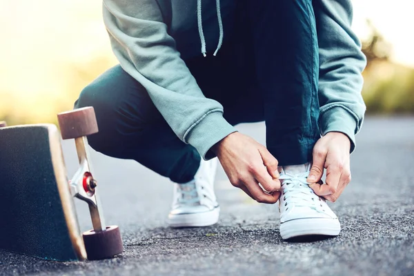 Hands, skater and man tie shoes on street to start fitness, training or workout. Sports, skateboarding and male with skateboard, tying sneaker laces on road and getting ready for exercise outdoors