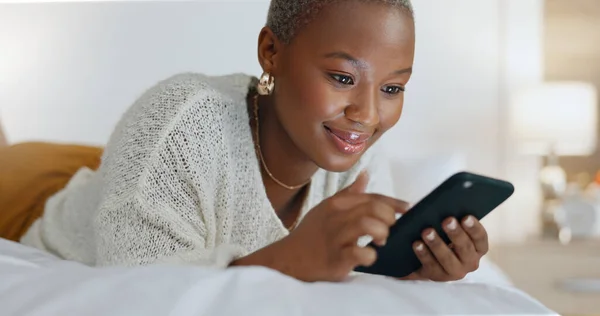 Social media phone, bed relax and black woman in communication on mobile app, reading notification on the web and happy with internet search on tech. African girl with technology in bedroom of house.