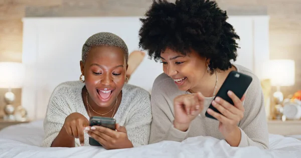 Friends, phone and girls night in bedroom on social media. Happy, smile and black woman on bed with friend watching funny video. Women at sleep over, reading and exited for online dating app message