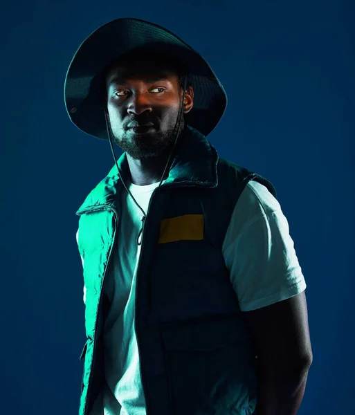 Fashion, shadow and black man model in a studio with a cool, stylish and casual outfit with lighting. Edgy, style and trendy fashionable African male posing while isolated by a blue background