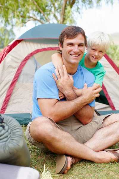 Father and son sitting in front of tent. Father and son camping with boy hugging his father from behind