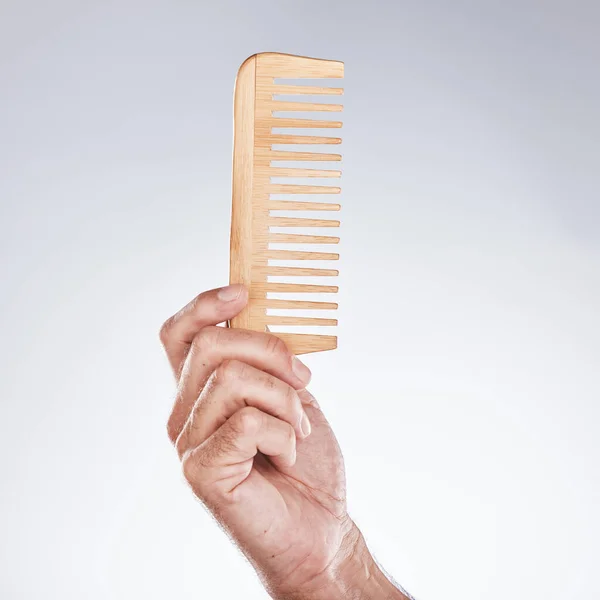 Hand, comb and haircare with a man barber in studio on a gray background for grooming or hair styling. Salon, bamboo and beauty with a male hairdresser holding a tool to groom or style closeup indoor.