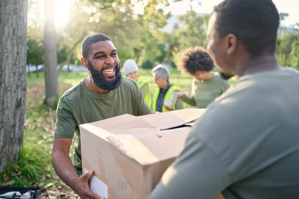 Community service, black man and giving box in park of donation, volunteering or social responsibility. Happy guy, NGO workers and helping with package outdoor of charity, support or society outreach.
