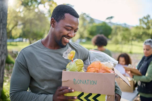 Food, donation and man in park with smile and grocery box, happy, healthy diet at refugee feeding project. Fresh fruit, charity donations and help to feed people, support from farm volunteer at ngo