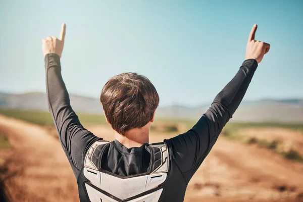 Winner, hands and back of a sports man outdoor on a dirt track for racing, competition or adrenaline. Success, celebration and winning with a male athlete or biker standing hands raised outside.