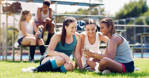 Sports, women and group outdoor, smartphone and connection with girls on field, chatting and relax. Fitness, female athletes smile and young ladies with cellphone, summer and on break after training.