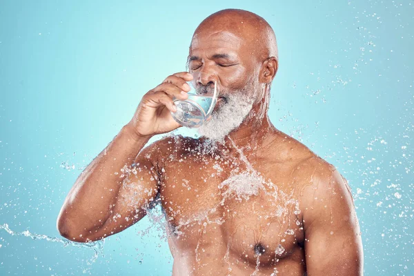 Drinking water, splash and skincare of black man in studio isolated on blue background. Wellness, cleaning and senior male model drink liquid for hydration, bathing and washing for health and hygiene.