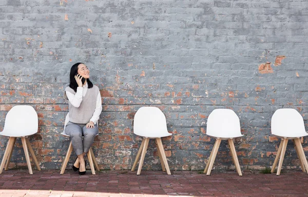 Phone call, thinking in waiting room and woman with chairs, job recruitment and employment with smile in Japan. Happy person sitting on chair with smartphone, smiling and talking with mockup space