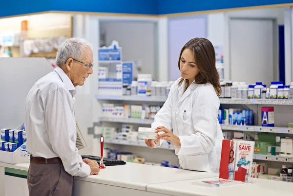 Providing customers with the medication they need. a young pharmacist helping an elderly customer at the prescription counter
