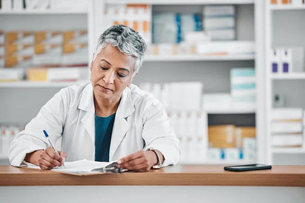 Senior woman, pharmacist writing and paper data of pharmacy stock or insurance documents. Healthcare, doctor and elderly female wellness consultant with store logistics research about shop products.