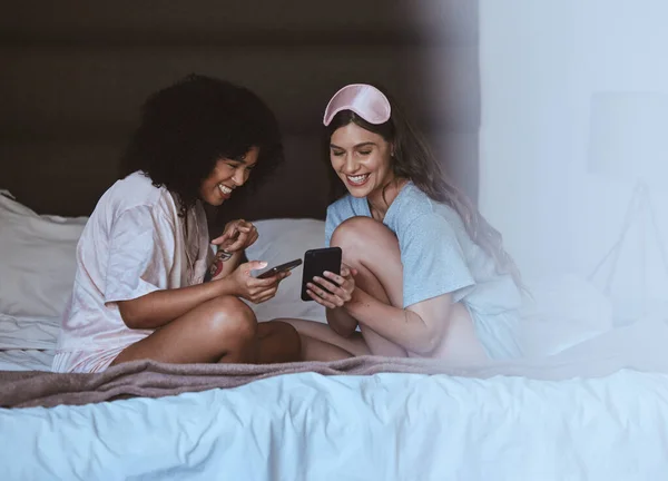 Woman, friends and phone with smile for social media, networking or funny meme on bed together at home. Happy women smiling, laughing and relaxing for post or smartphone entertainment in the bedroom.