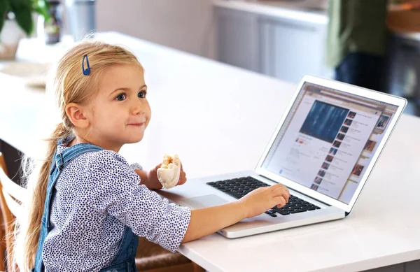 Getting an early start on her IT career. a cute little girl using a laptop while having a snack