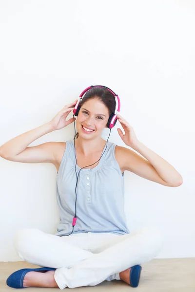 Portrait, music and woman on a floor with headphones in studio, happy and streaming on a wall background. Face, smile and girl relax with podcast, radio or audio track while sitting against mockup.