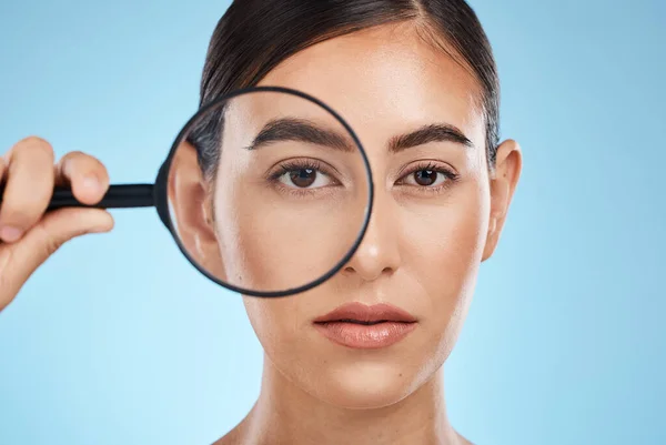 Woman, face with magnifying glass, eyes and beauty in portrait, eye care and vision isolated on blue background. Skincare cosmetics, skin and facial inspection, mockup space and dermatology in studio.