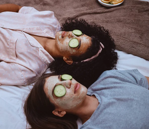Facial, cucumber and sleepover with girl best friends lying on the floor together for beauty treatment. Face mask, skincare or natural care with a female and friend at home to relax while bonding.