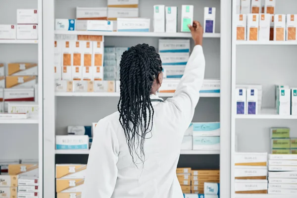 Choice, back and pharmacist at a shelf for medicine, inventory and check on pills in a clinic. Medical, healthcare and black woman working with medication at a phamacy for service, health and work.