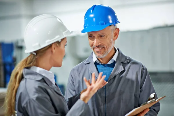 Creating good work relationships. Two factory employees wearing hardhats having a discussion