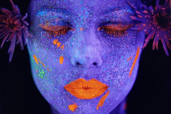 Treasures in the dark. a young woman posing with neon paint on her face