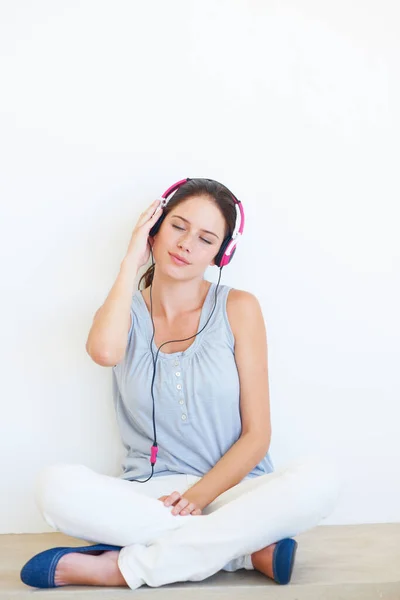 Relax, music and woman on a floor with headphones in studio, happy and streaming on a wall background. Zen, feeling and girl with wellness podcast, radio or audio track while sitting against mockup.
