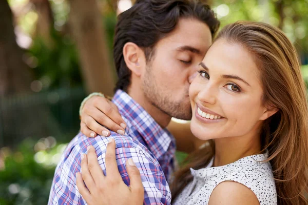 Couple portrait, hug or cheek kiss on romance date, love or valentines day in park, backyard bonding or relax garden. Smile, man or woman embrace in honeymoon trust, support or security on holiday.