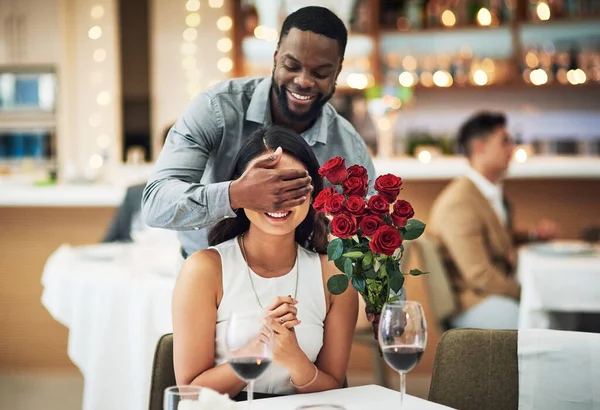 Rose surprise, couple and restaurant of people ready for fine dining with love and care. Flowers present, bouquet and date of a woman and man together with celebration on a table with a smile.