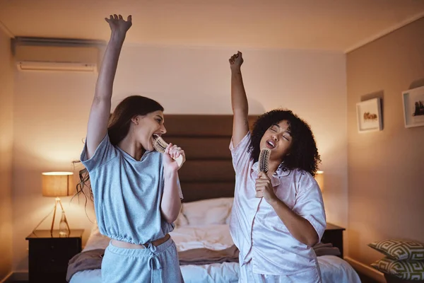 Friends, singing with brush and women in pajamas to get ready for girls night out dancing, fun music concert and happiness. Girl, friend and happy smile, girlfriends karaoke at sleepover in bedroom