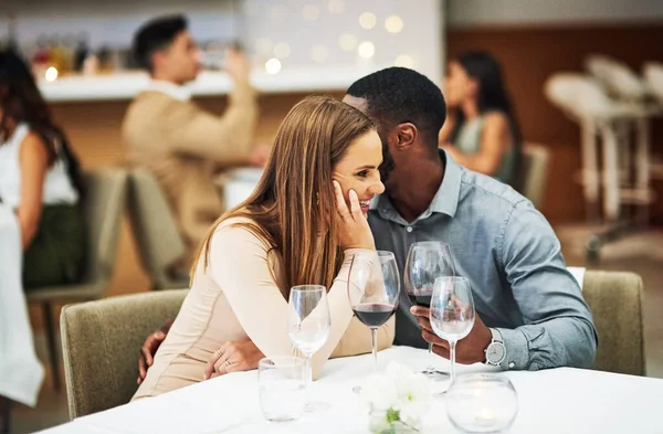 Love, man whisper with woman and in restaurant with wine glasses, happiness or cheerful on Valentines day. Romance, couple or flirty for quality time, romantic or conversation with fine dining or joy.