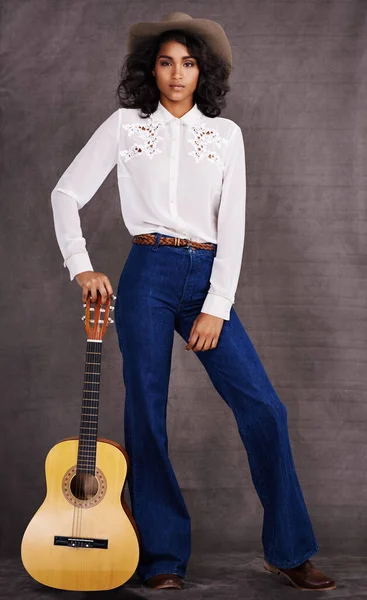 In tune with my heritage. a beautiful fashion model in a western outfit posing with a guitar against a gray background
