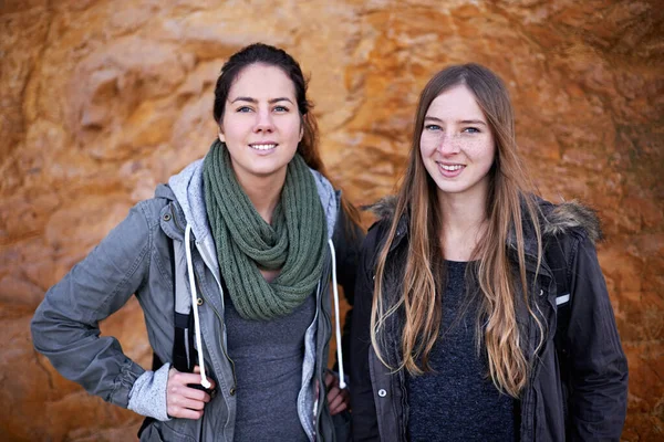 They share a love of the outdoors. Portrait of two attractive young female hikers standing by a rockface