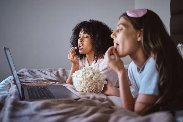 Laptop, movie and relax with friends and popcorn in bedroom for sleepover, bonding and streaming. Technology, internet and online with women at night for cinema, subscription and film entertainment.