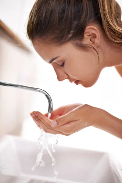 Beautiful skin begins with washing. Closeup shot of a young woman washing her face over a sink