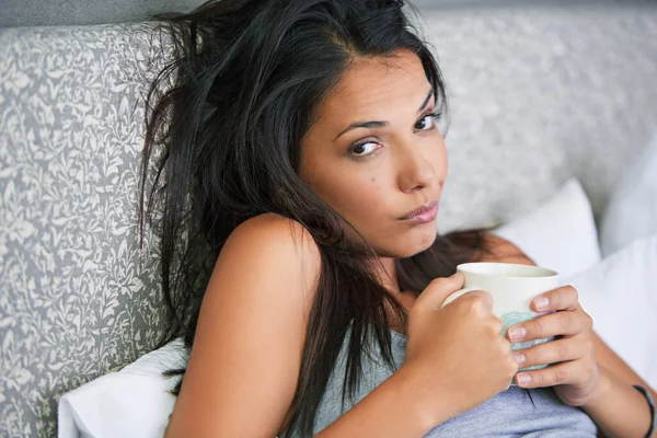 I dont wanna get up...Portrait of a young woman drinking coffee while looking tired in bed
