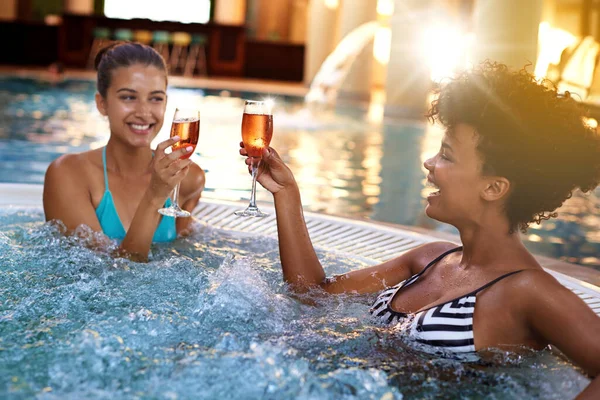 But first, champagne. two young women enjoying a glass of champagne in a jacuzzi