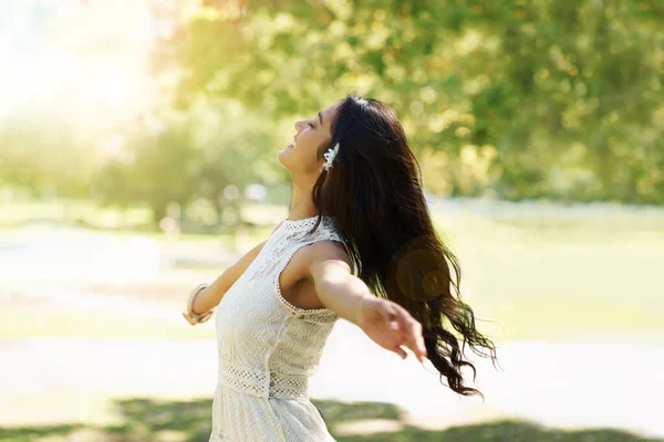 Free your spirit in the spring air. A young woman twirling in a park with her arms outstretched