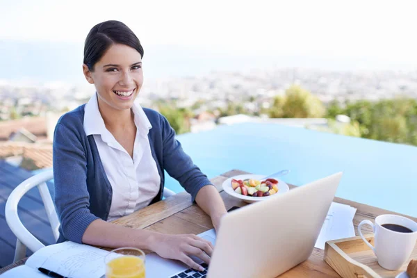 she works where ever she goes. a young businesswoman working on her laptop by a swimming pool