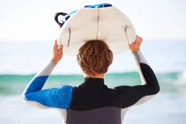 Surfing, sports and man by sea for fitness, exercise or training and walking to ocean water. Surfboard and super, person or rear of professional athlete with wellness, health and beach waves activity.