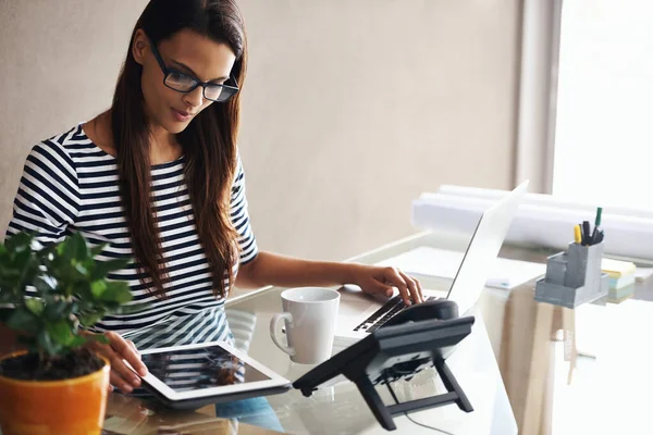 Doing business digitally. a young businesswoman sitting at her desk using a laptop and digital tablet