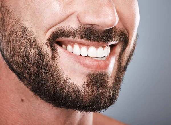 Smile, dental health and mouth of a man with teeth isolated on grey studio background. Happy, showing and beard of a model with results from tooth whitening, dentist cleaning and hygiene on backdrop.